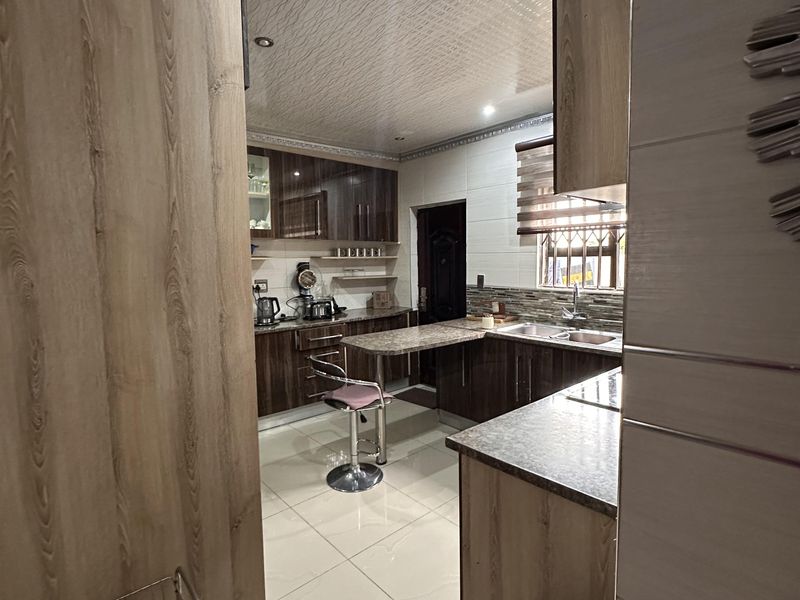 A functional kitchen featuring wood-finish cabinetry, laminate countertops, a breakfast bar, and tiled flooring with a textured ceiling finish.
