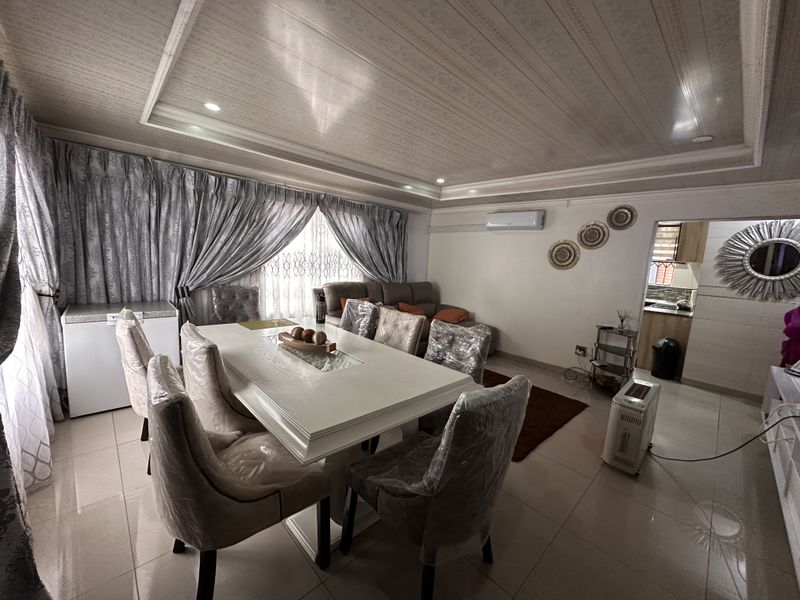Open-plan living and dining area featuring tiled floors, a recessed ceiling with cove lighting, and a split-system air conditioner, with an adjacent kitchen.