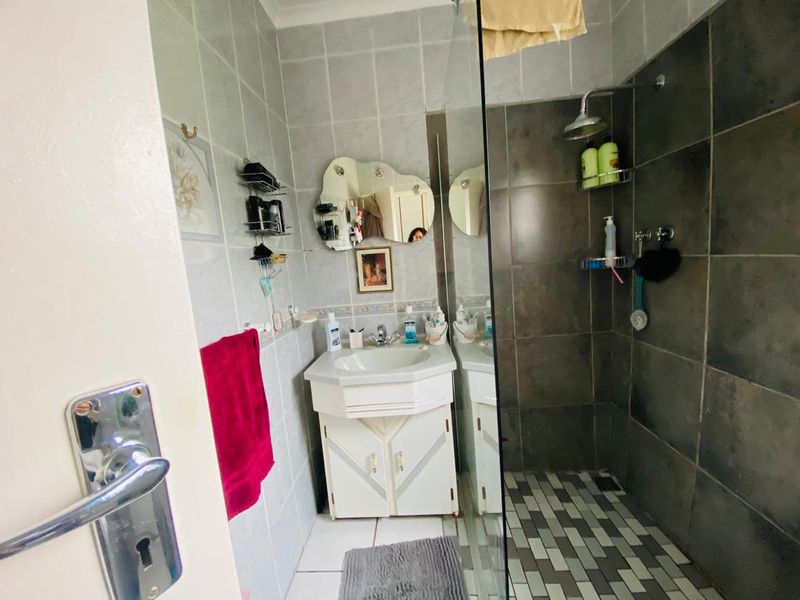 A functional bathroom featuring a vanity cabinet with basin, wall-mounted mirror, and a walk-in shower with glass screen and tiled finishes.