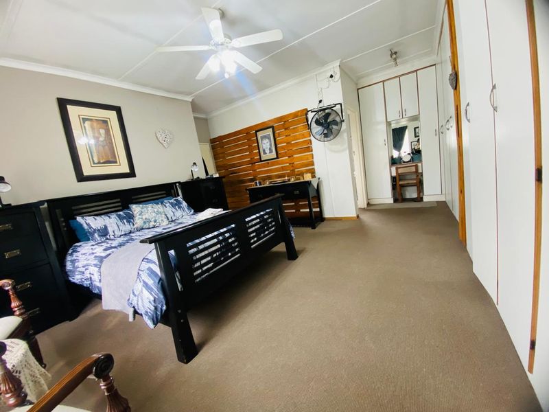 Spacious bedroom featuring built-in cupboards, carpeted flooring, and a ceiling fan, offering a comfortable and functional living space.