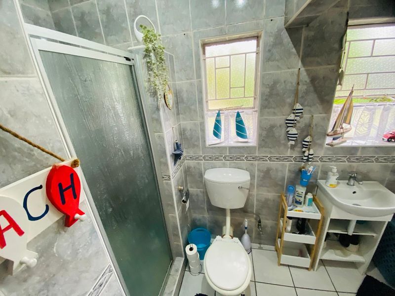 A functional bathroom featuring a shower enclosure, pedestal basin, and toilet, finished with neutral wall and floor tiling.