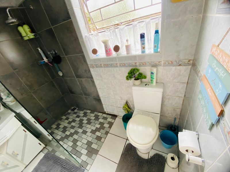 Compact bathroom featuring a walk-in shower with glass screen, tiled walls and flooring, and a standard toilet.