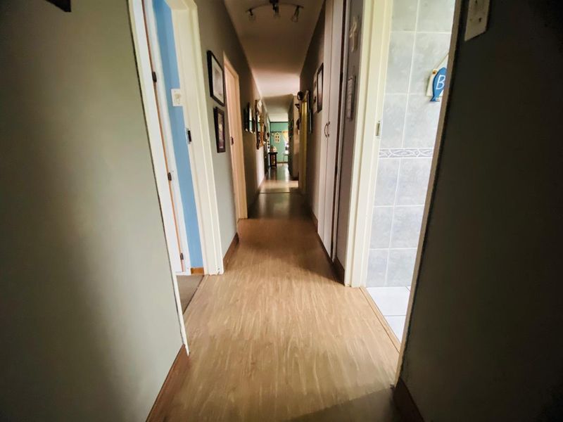 A functional hallway featuring laminate flooring, built-in storage cupboards, and overhead track lighting, providing access to adjacent rooms.