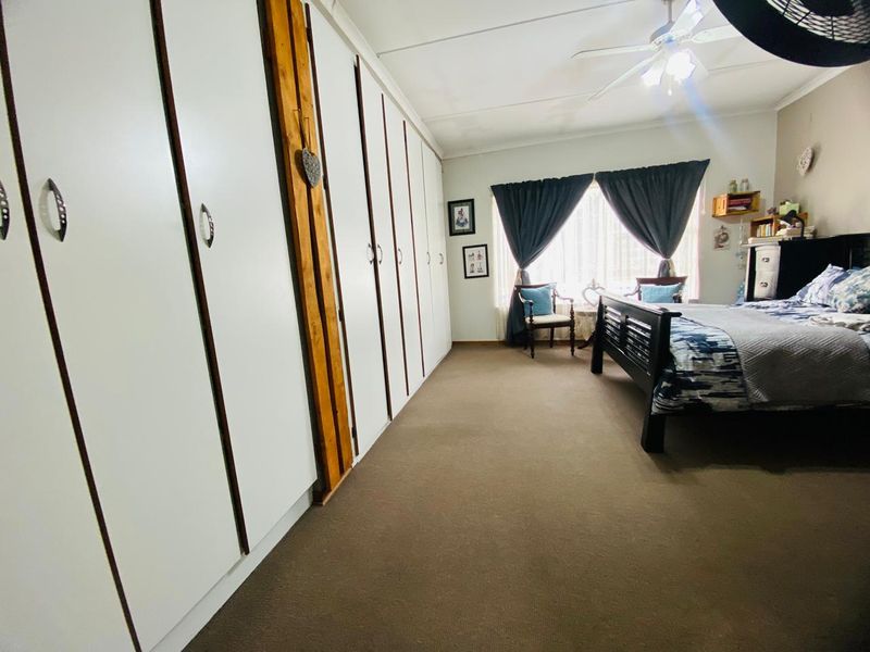 Spacious bedroom featuring extensive built-in cupboards, carpeted flooring, and a ceiling fan, offering ample storage and comfortable living space.