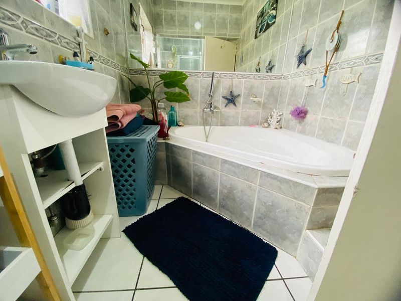 A functional bathroom featuring a built-in bathtub with shower mixer, tiled wall finishes, and a vanity basin.