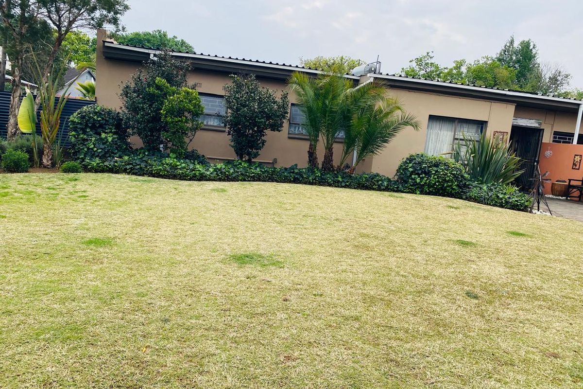 A view of the rear exterior of the house featuring a well-maintained lawn, landscaped garden beds, and a solar geyser installed on the roof.