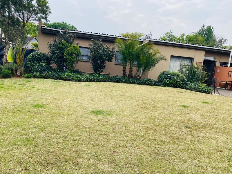 A view of the rear exterior of the house featuring a well-maintained lawn, landscaped garden beds, and a solar geyser installed on the roof.