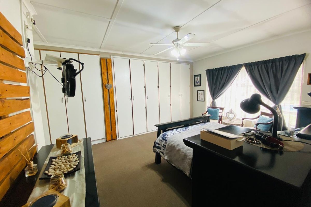 A spacious bedroom featuring extensive built-in cupboards, a ceiling fan, and neutral carpeting, offering ample storage and a comfortable living environment.