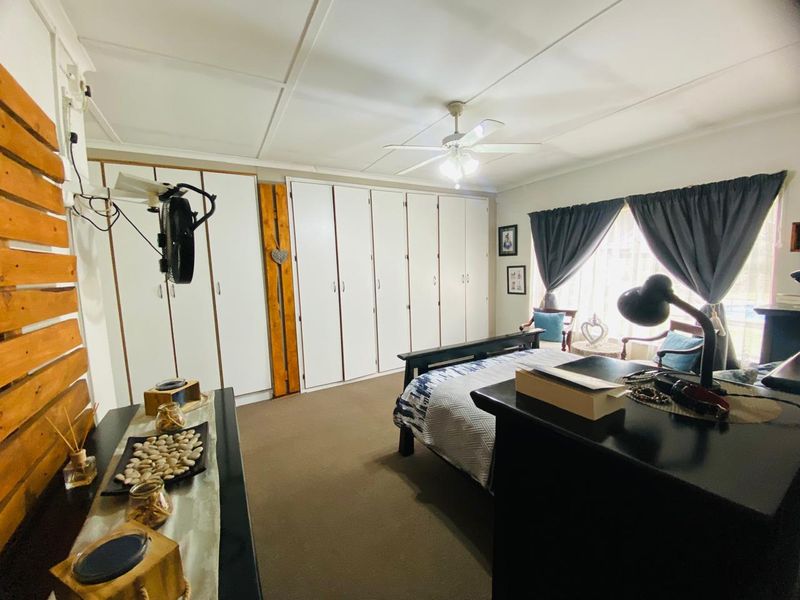 A spacious bedroom featuring extensive built-in cupboards, a ceiling fan, and neutral carpeting, offering ample storage and a comfortable living environment.