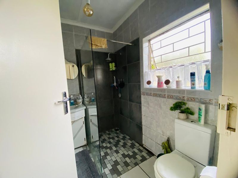 A functional bathroom featuring a walk-in shower with a glass screen, a vanity cabinet, and a toilet, finished with tiled walls and flooring.