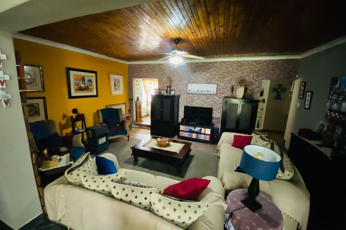 A living room featuring a timber tongue and groove ceiling, ceiling fan, and an exposed brick feature wall with tiled flooring.