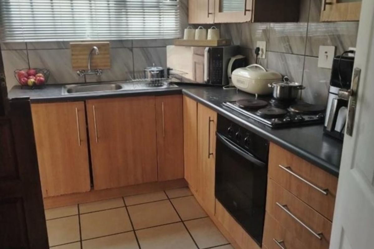 A functional kitchen featuring wood-finish cabinetry, dark countertops, built-in oven and hob, tiled flooring, and a window with security bars.