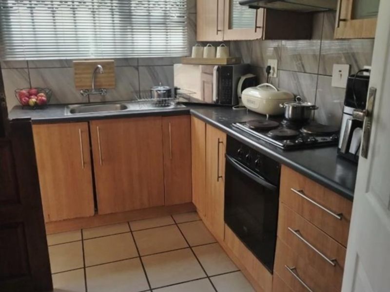 A functional kitchen featuring wood-finish cabinetry, dark countertops, built-in oven and hob, tiled flooring, and a window with security bars.