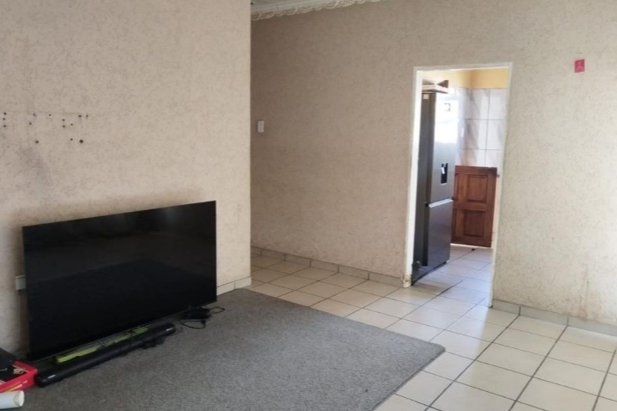 A living room area featuring tiled flooring and ceiling cornicing, leading through to an adjacent room.