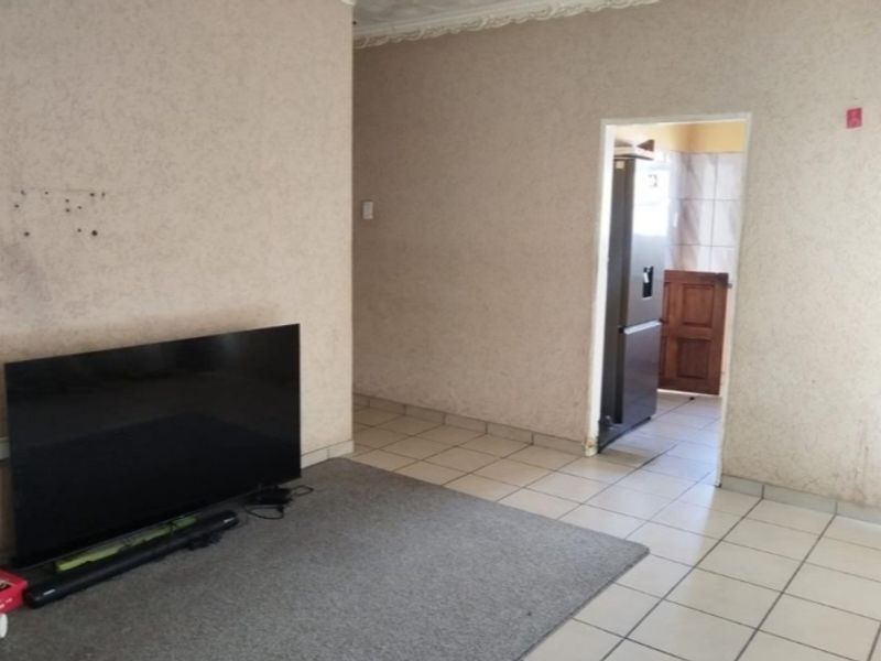 A living room area featuring tiled flooring and ceiling cornicing, leading through to an adjacent room.