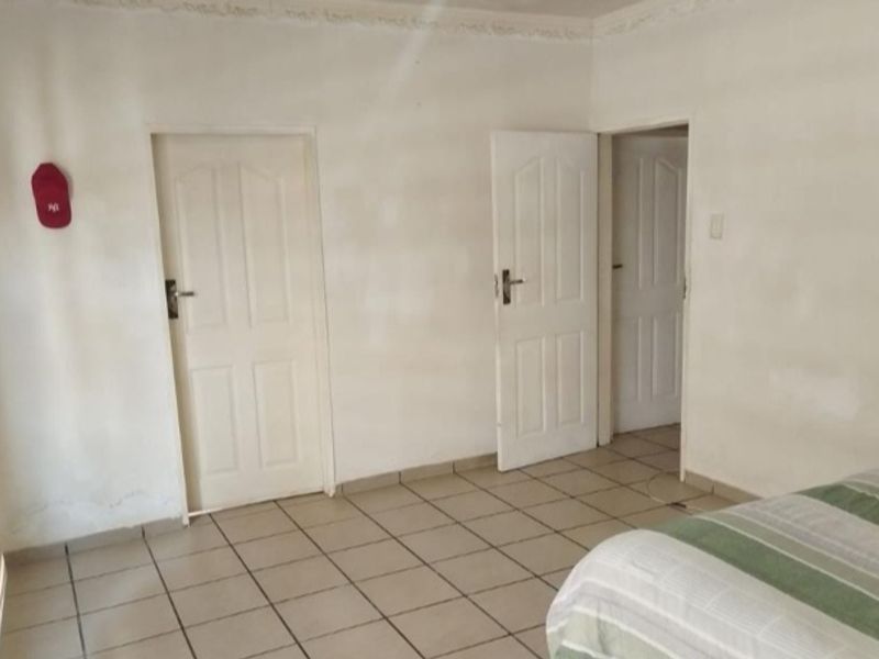 A bedroom featuring tiled flooring, decorative cornicing, and multiple panel doors, requiring cosmetic updates to the wall finishes.