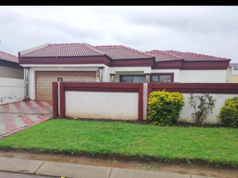 Front elevation of a single-story house featuring a tiled roof, integrated garage, and a front boundary wall with a paved driveway.
