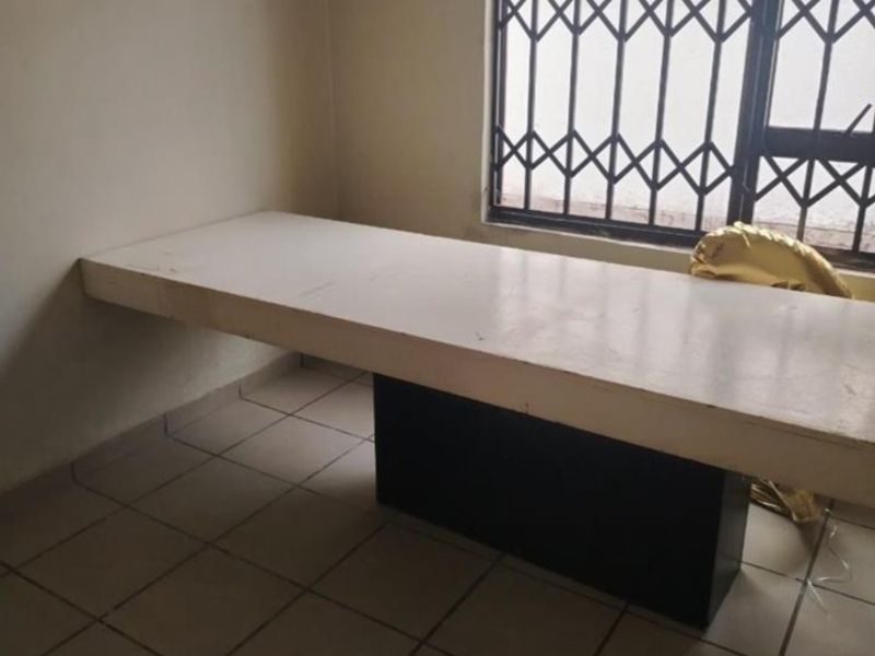 A sparse bedroom featuring a built-in desk, tiled flooring, and a window fitted with a security gate.