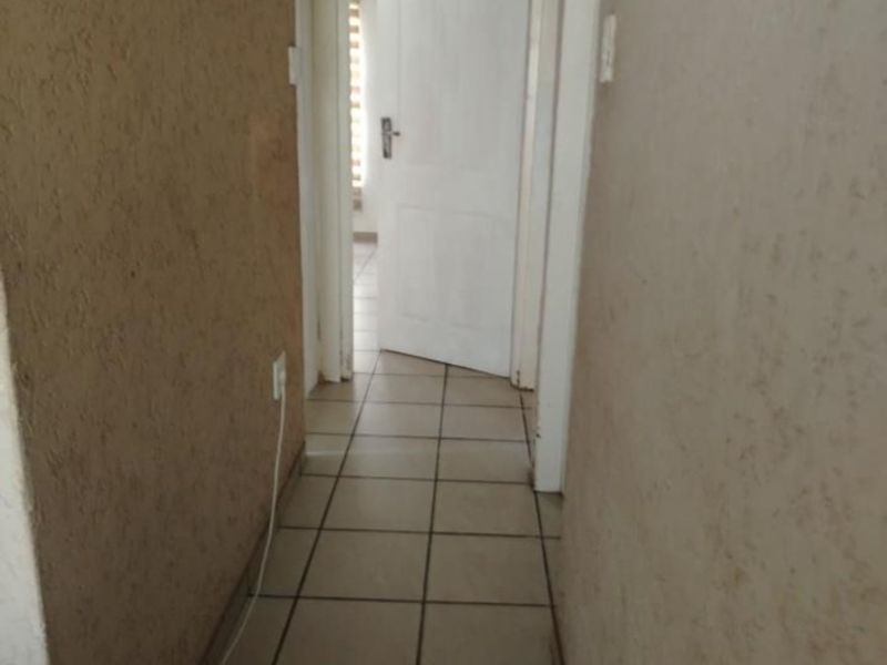 A functional hallway featuring tiled flooring and textured wall finishes, providing access to multiple rooms within the property.