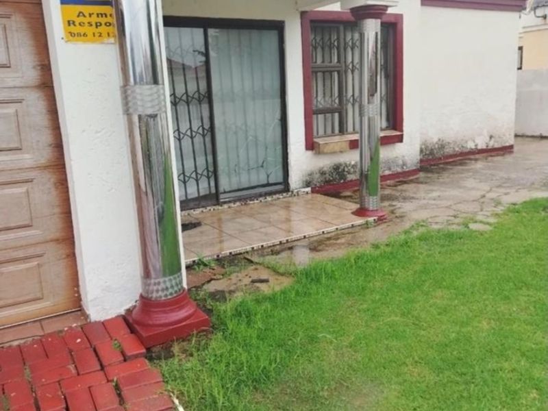 Front entrance area featuring a tiled porch, decorative columns, and sliding door access, with visible signs of exterior wall weathering and paving maintenance required.