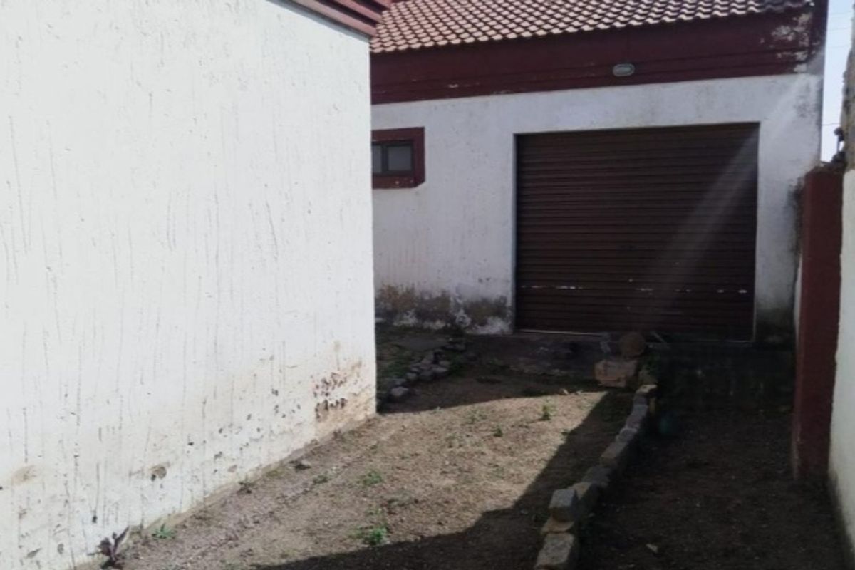 Rear exterior view showing a garage with a roller door and an unpaved yard area requiring maintenance and landscaping.