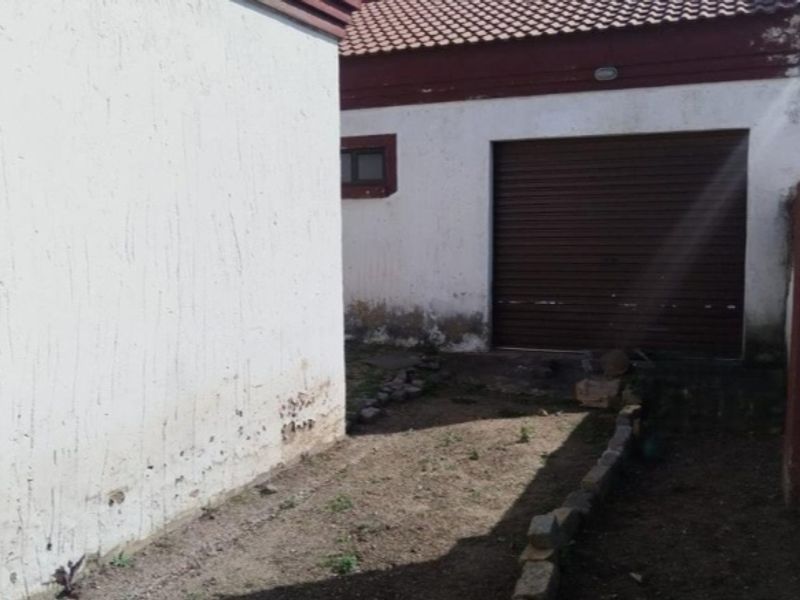 Rear exterior view showing a garage with a roller door and an unpaved yard area requiring maintenance and landscaping.