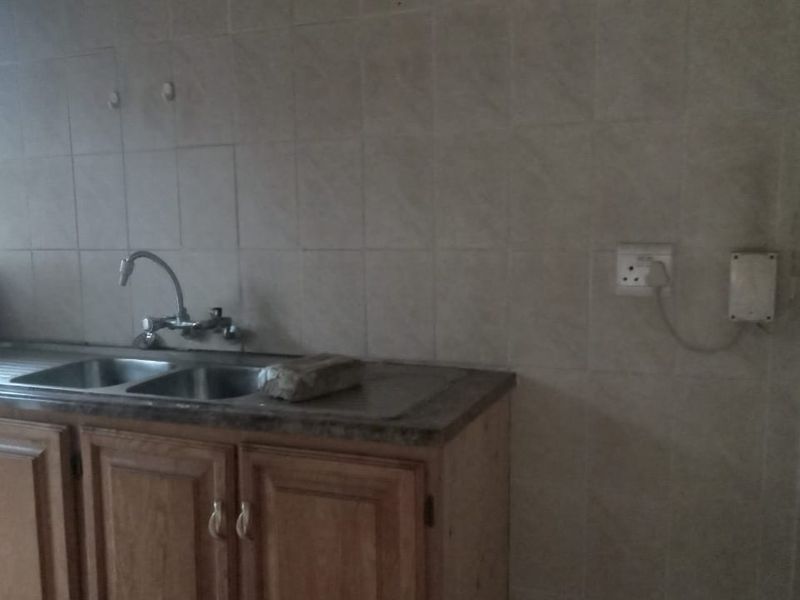 A functional kitchen area featuring wooden cabinetry, a double bowl stainless steel sink, and tiled splashback, offering potential for modernization.