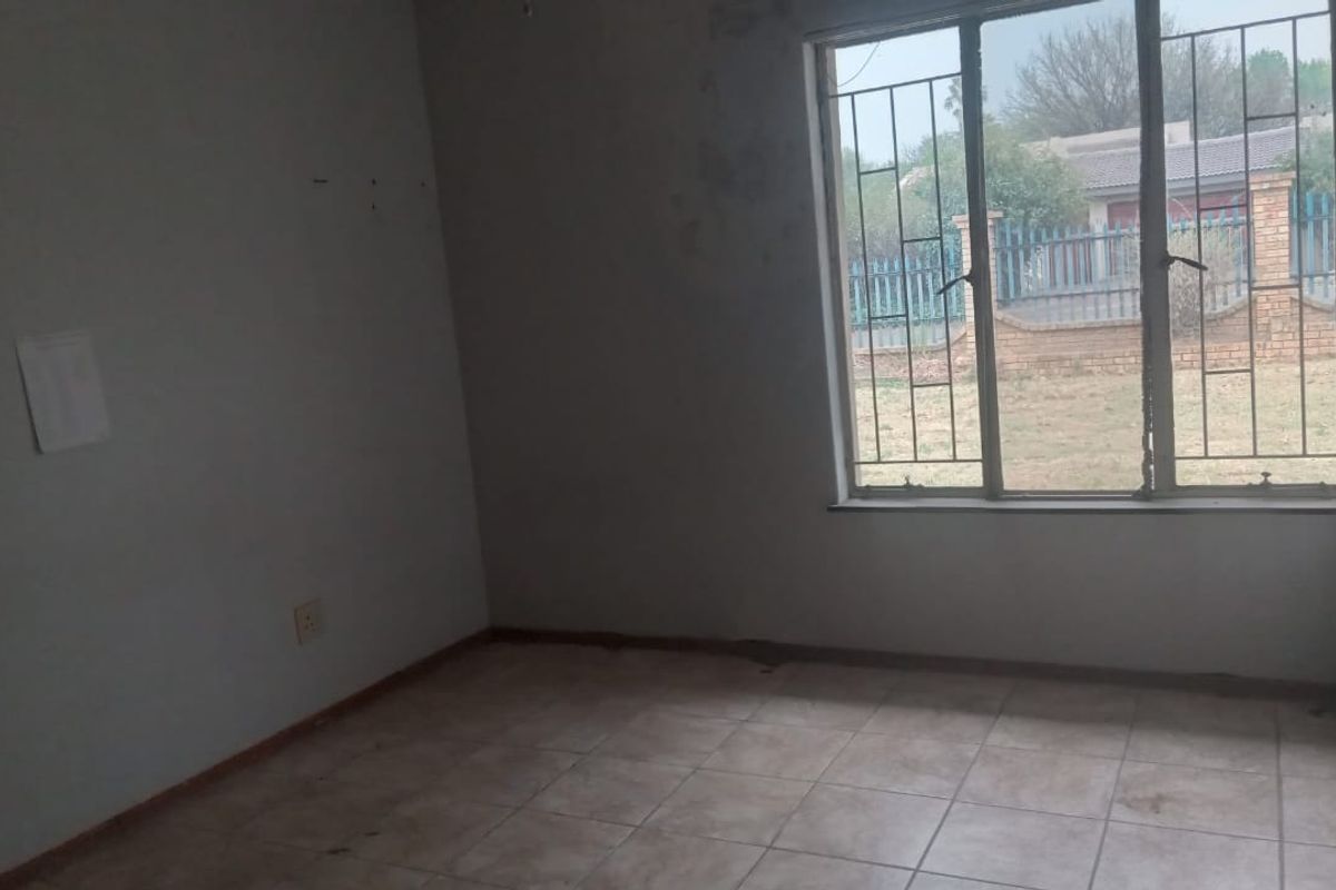 An empty bedroom featuring tiled flooring and security bars on the window, requiring cosmetic updates to the walls and flooring.