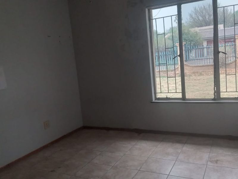 An empty bedroom featuring tiled flooring and security bars on the window, requiring cosmetic updates to the walls and flooring.