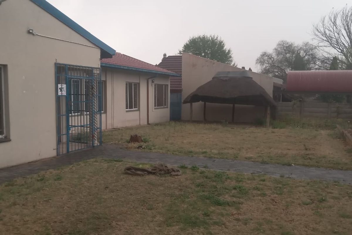 Rear exterior view of the property featuring a lawn, paved walkway, and a thatched lapa structure.