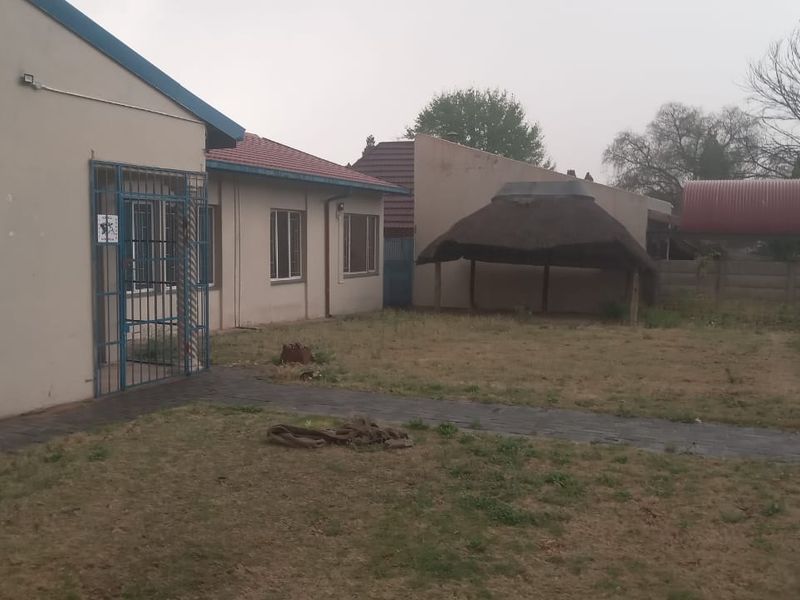 Rear exterior view of the property featuring a lawn, paved walkway, and a thatched lapa structure.