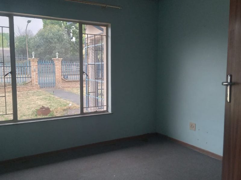 An empty bedroom featuring carpet flooring, security bars on the window, and a view of the front garden area.