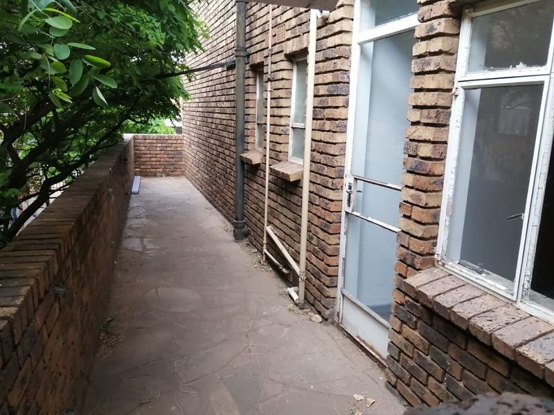 A narrow outdoor balcony featuring exposed brick walls, stone paving, and metal-framed access points, providing a functional exterior space.