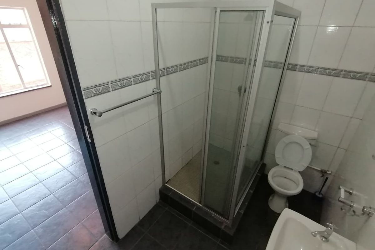 A functional bathroom featuring a shower enclosure, toilet, and pedestal basin with tiled walls and flooring.