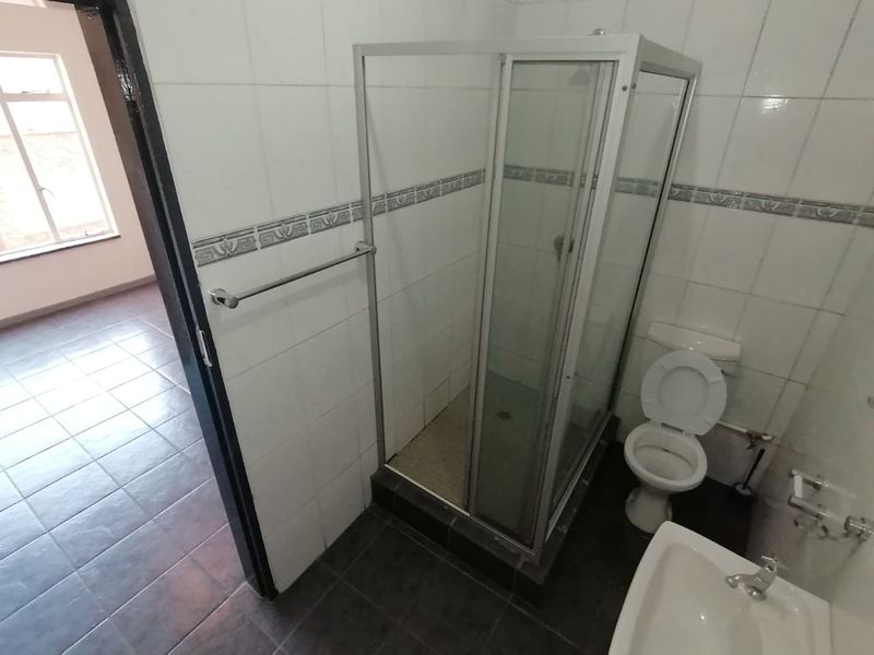 A functional bathroom featuring a shower enclosure, toilet, and pedestal basin with tiled walls and flooring.