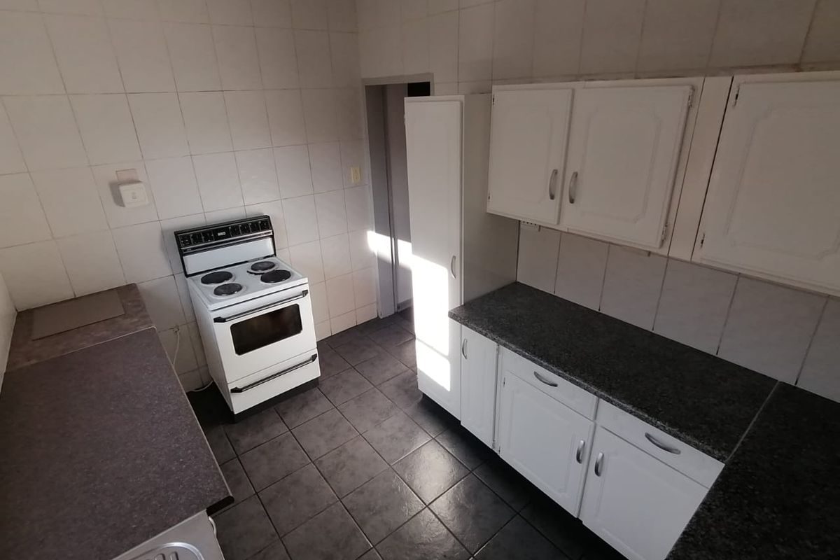 A functional kitchen featuring white cabinetry, dark laminate countertops, tiled backsplash, and tiled flooring, providing a clean and practical workspace.