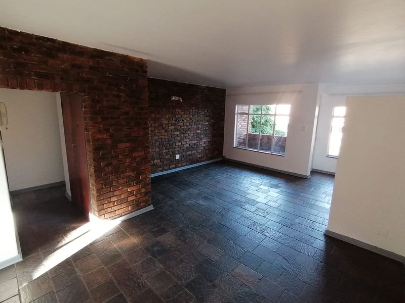 Spacious living area featuring a rustic exposed brick wall and durable slate tile flooring, offering a bright and open layout.