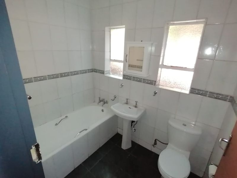 A dated bathroom featuring a standard bathtub, pedestal basin, and toilet with white wall tiles and dark floor tiles.