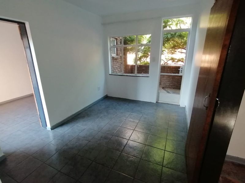 An empty bedroom featuring dark tiled flooring, a built-in cupboard, and natural light through a large window and glass panel door.
