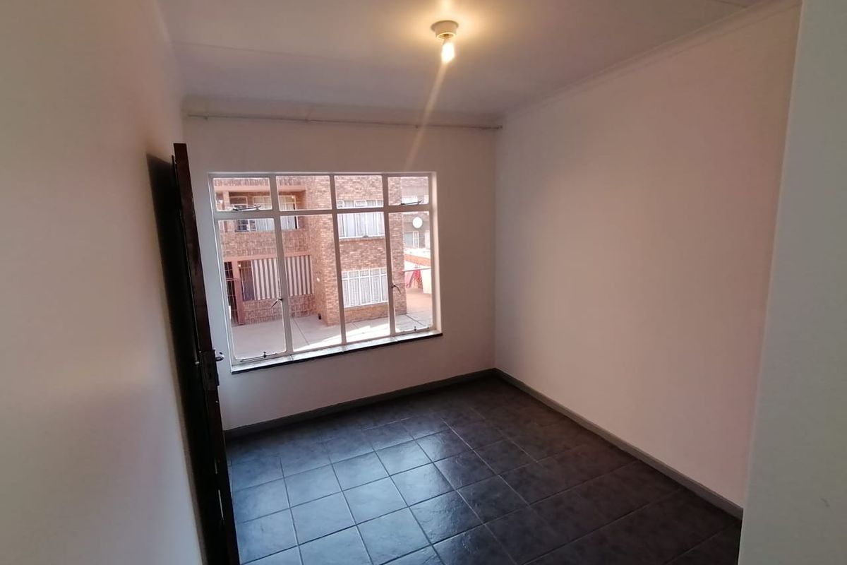 A clean, empty bedroom featuring dark tiled flooring, neutral walls, and a large window providing natural light.