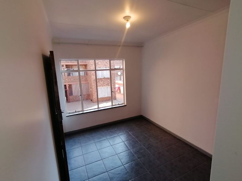 A clean, empty bedroom featuring dark tiled flooring, neutral walls, and a large window providing natural light.
