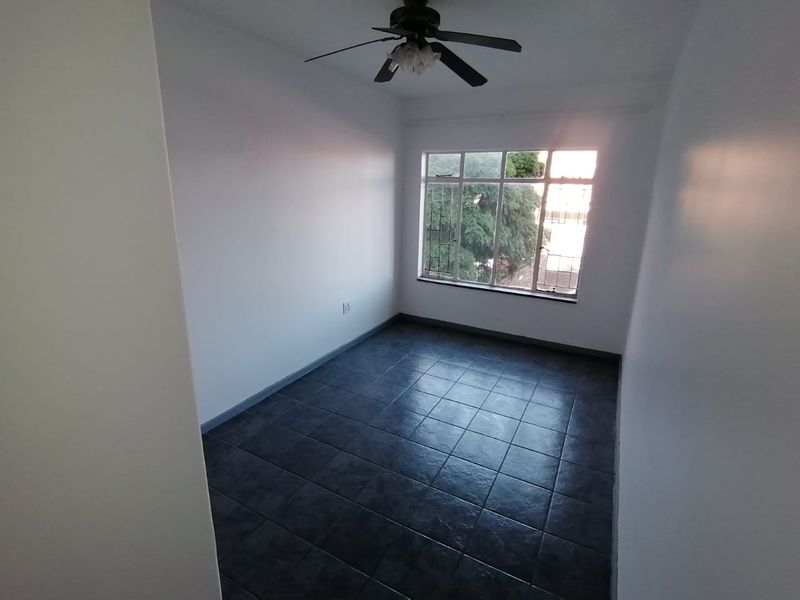A vacant bedroom featuring dark tiled flooring, a ceiling fan, and a window with security bars, offering a clean and neutral space.