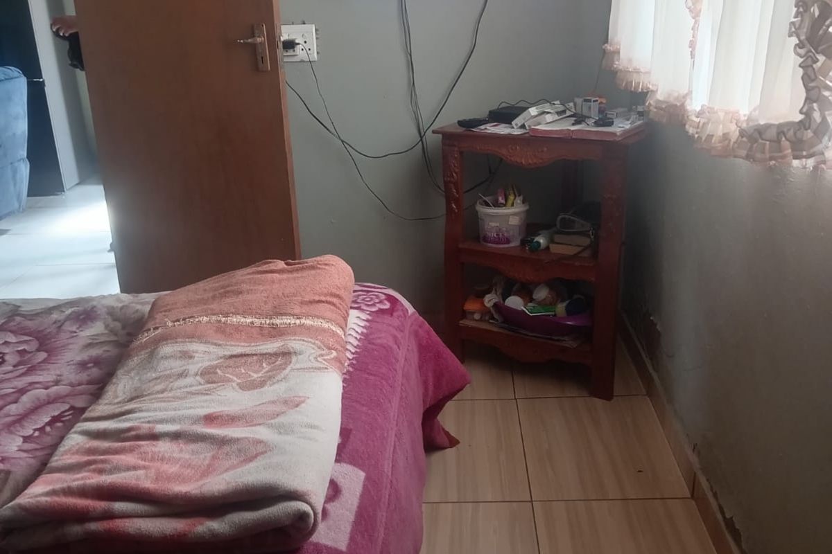 A bedroom featuring tiled flooring and curtain rails, showing signs of wall dampness and requiring maintenance to address exposed wiring and finishings.