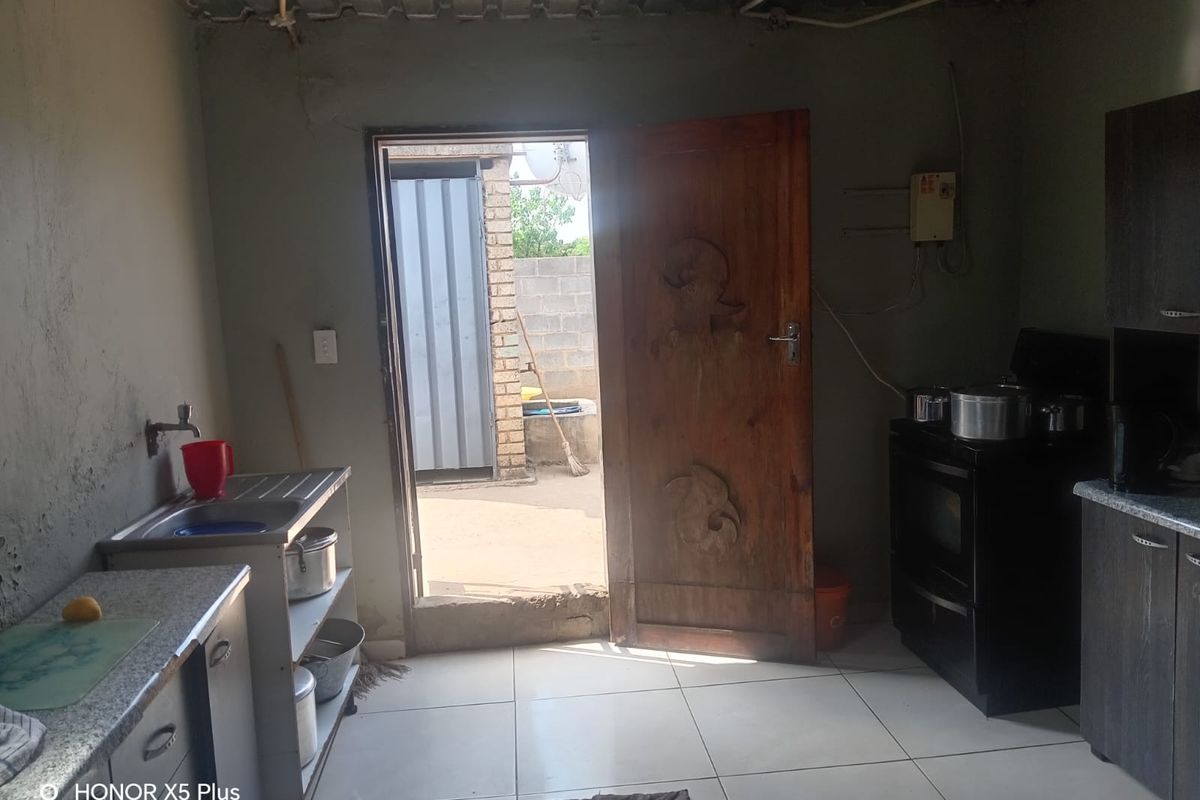 A functional kitchen area featuring tiled floors, built-in cabinetry, and a stainless steel sink, with direct access to an outdoor space.
