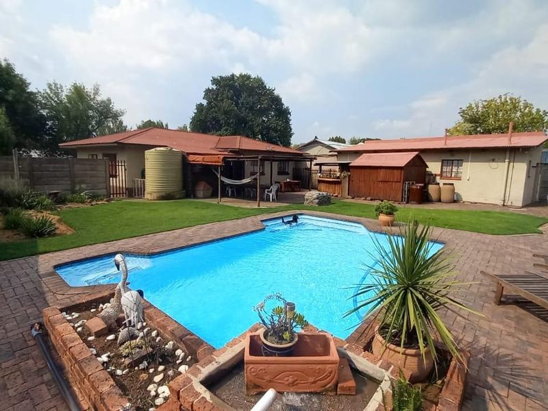 Spacious backyard featuring a swimming pool, brick-paved surround, manicured lawn, and a covered patio area, ideal for outdoor entertaining.
