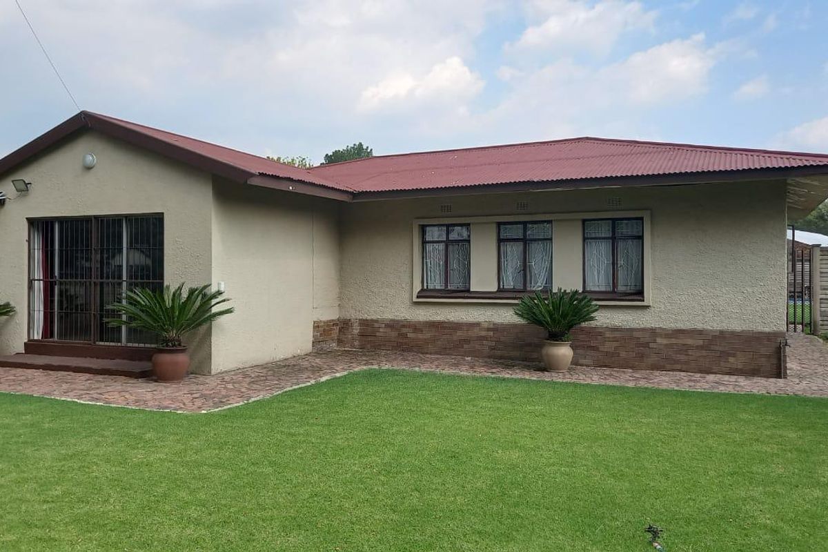 Rear view of the house featuring a corrugated metal roof, brick-accented facade, sliding glass doors with security bars, and a well-maintained lawn.