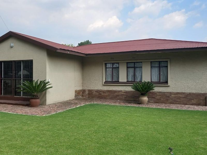 Rear view of the house featuring a corrugated metal roof, brick-accented facade, sliding glass doors with security bars, and a well-maintained lawn.