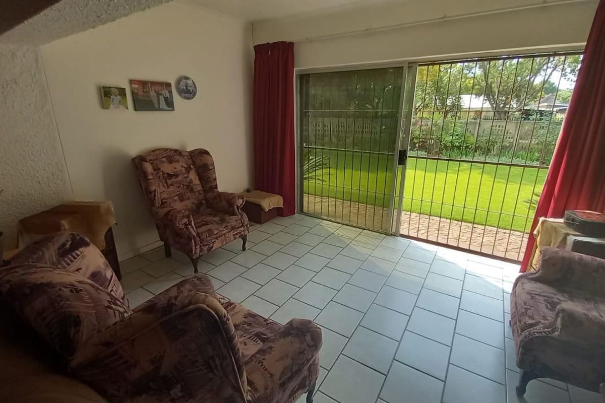 A living room featuring tiled flooring, a textured ceiling, and a sliding glass door with a security gate leading to the garden.