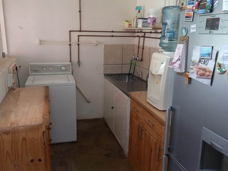 A functional laundry area featuring built-in cabinetry, a stainless steel sink, and exposed plumbing, providing a practical space for utility and washing needs.