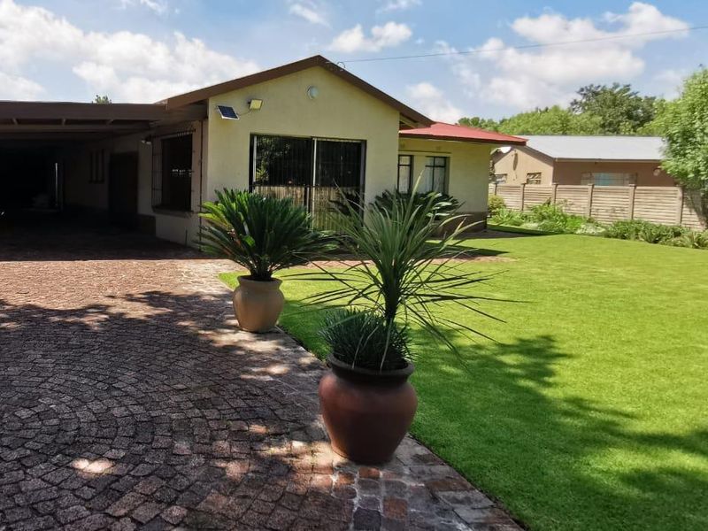 Front view of the property featuring a paved driveway, attached carport, well-maintained lawn, and secure boundary walling.